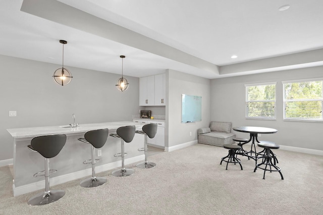 kitchen with a kitchen breakfast bar, white cabinetry, pendant lighting, and light colored carpet