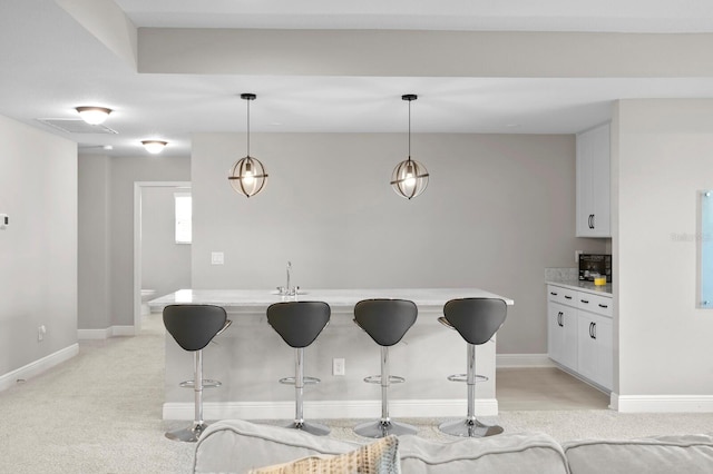 kitchen with white cabinetry, a breakfast bar area, pendant lighting, sink, and light colored carpet