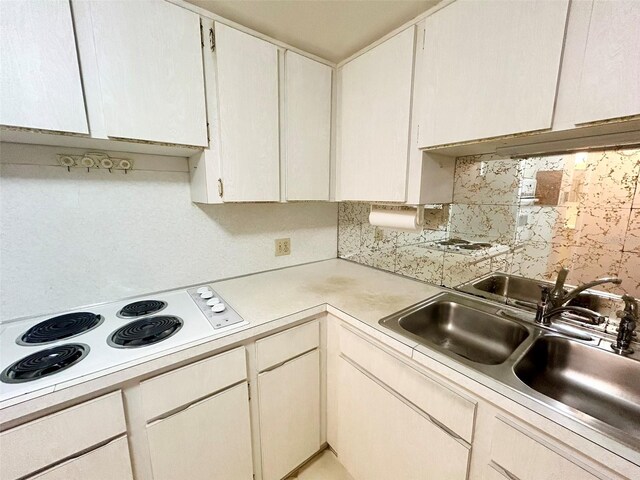 kitchen with white electric stovetop, sink, decorative backsplash, and white cabinetry