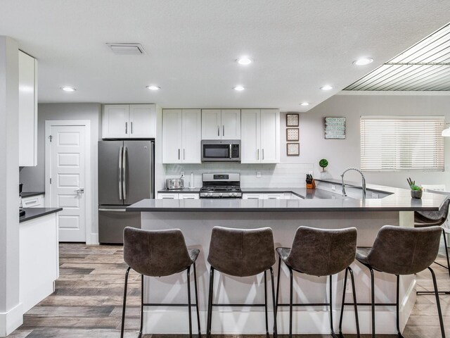 kitchen featuring a breakfast bar, hardwood / wood-style flooring, white cabinetry, kitchen peninsula, and appliances with stainless steel finishes