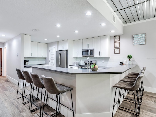 kitchen featuring kitchen peninsula, white cabinetry, appliances with stainless steel finishes, a kitchen breakfast bar, and light hardwood / wood-style floors