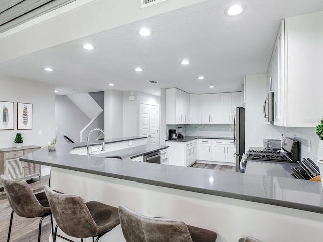 kitchen featuring white cabinets, stainless steel appliances, kitchen peninsula, and decorative backsplash