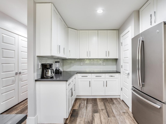 kitchen featuring stainless steel fridge, white cabinetry, decorative backsplash, and light hardwood / wood-style flooring