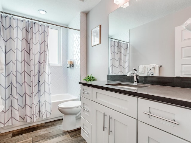 full bathroom with vanity, wood-type flooring, a textured ceiling, shower / bath combo with shower curtain, and toilet