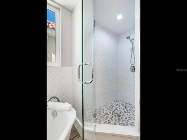 bathroom featuring plus walk in shower and tile walls