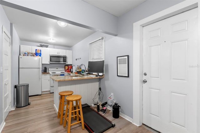 kitchen featuring white cabinets, white appliances, kitchen peninsula, a kitchen bar, and light hardwood / wood-style flooring