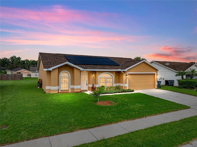 ranch-style home with a garage, solar panels, and a yard