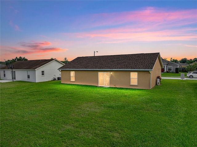 back house at dusk featuring a lawn