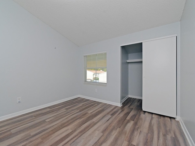 unfurnished bedroom with a textured ceiling, lofted ceiling, dark wood-type flooring, and a closet