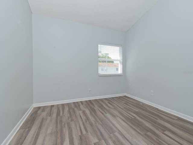 empty room with light wood-type flooring, lofted ceiling, and a textured ceiling