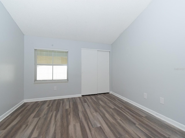 unfurnished bedroom featuring a textured ceiling, lofted ceiling, a closet, and dark hardwood / wood-style flooring