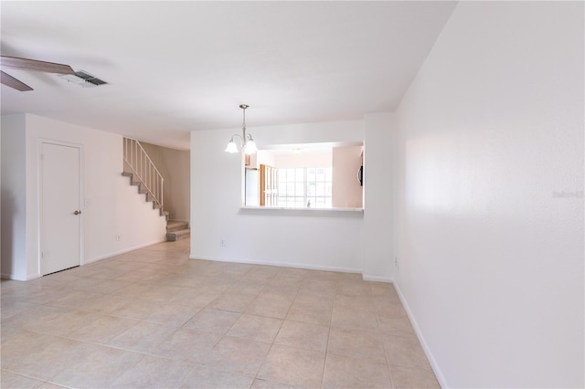 tiled empty room with ceiling fan with notable chandelier