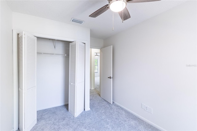 unfurnished bedroom with ceiling fan, light colored carpet, a textured ceiling, and a closet