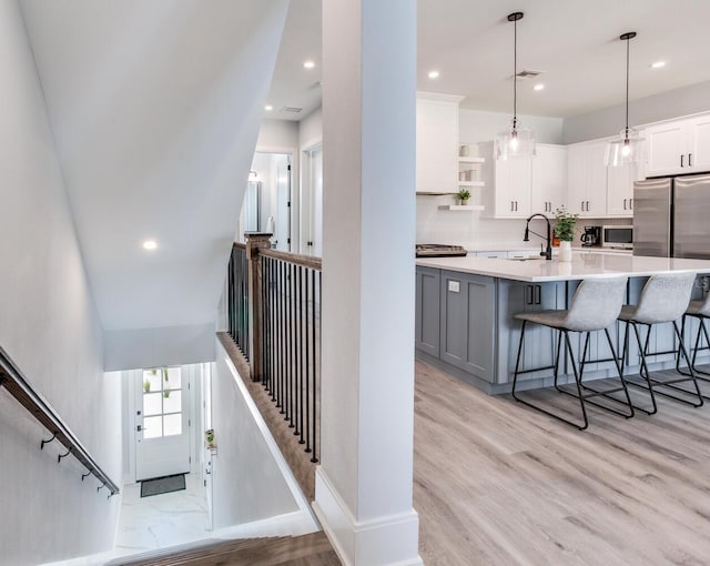 interior space with hanging light fixtures, white cabinetry, a breakfast bar area, gray cabinets, and light hardwood / wood-style flooring