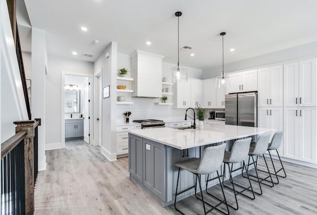 kitchen featuring an island with sink, white cabinetry, light hardwood / wood-style flooring, appliances with stainless steel finishes, and decorative light fixtures