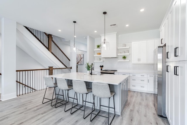 kitchen featuring white cabinets, pendant lighting, a kitchen island with sink, stainless steel appliances, and light hardwood / wood-style floors