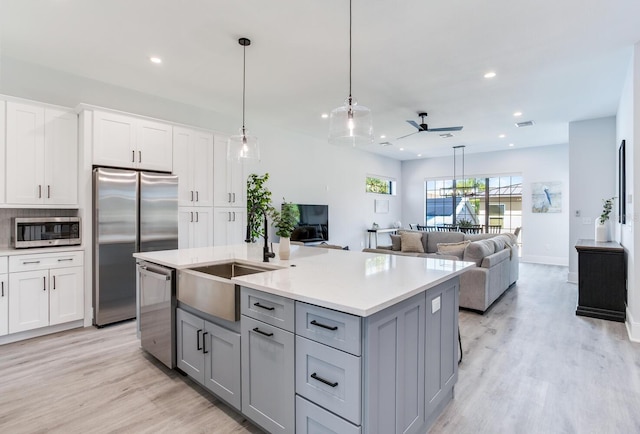 kitchen featuring gray cabinets, stainless steel appliances, ceiling fan, and a kitchen island with sink