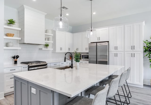 kitchen with light stone counters, pendant lighting, sink, white cabinetry, and stainless steel appliances