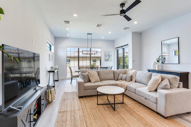 living room featuring ceiling fan with notable chandelier and light wood-type flooring