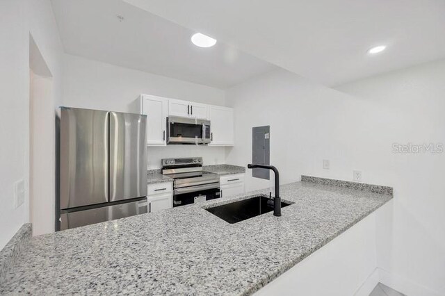 kitchen featuring kitchen peninsula, sink, stainless steel appliances, and light stone counters