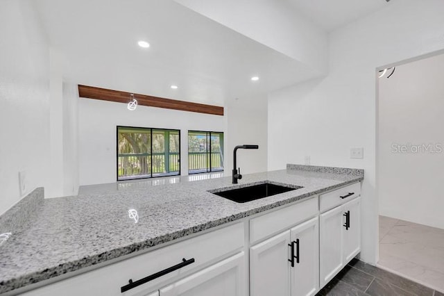 kitchen with light stone counters, kitchen peninsula, white cabinetry, and sink