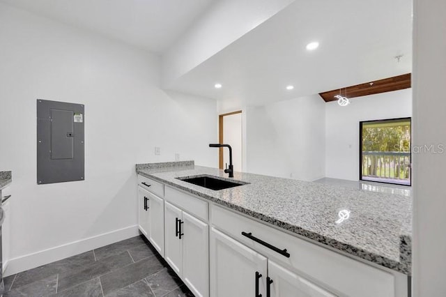 kitchen featuring white cabinetry, light stone counters, electric panel, kitchen peninsula, and sink