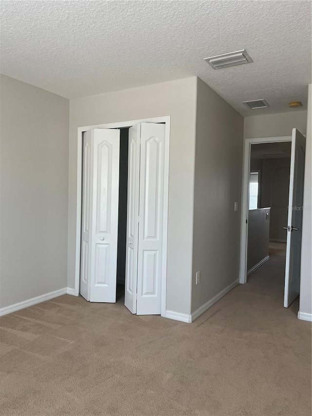 unfurnished bedroom with light colored carpet, a textured ceiling, and a closet