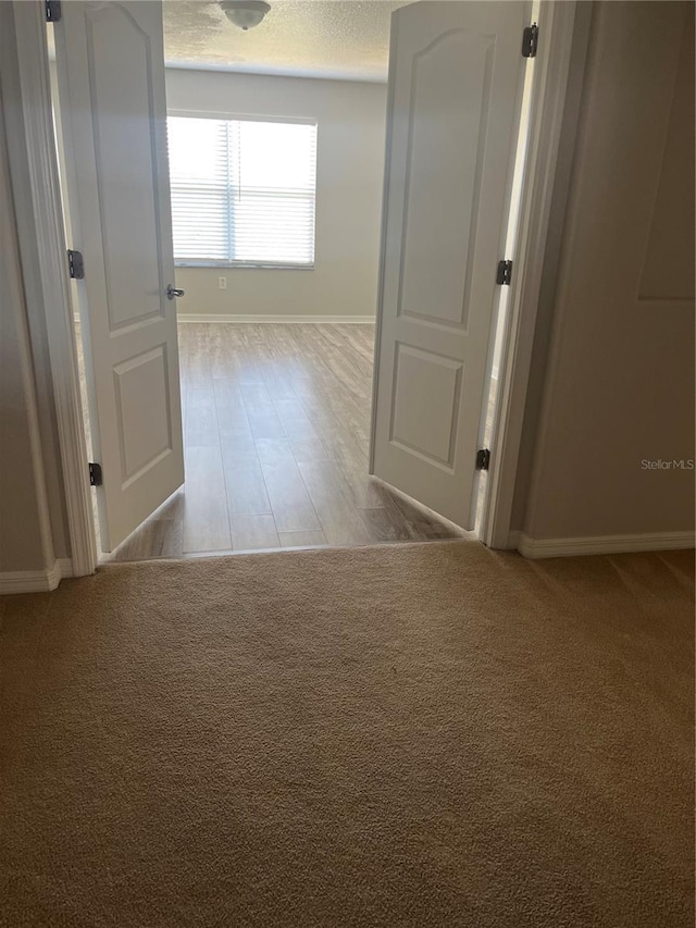 hall with light colored carpet and a textured ceiling