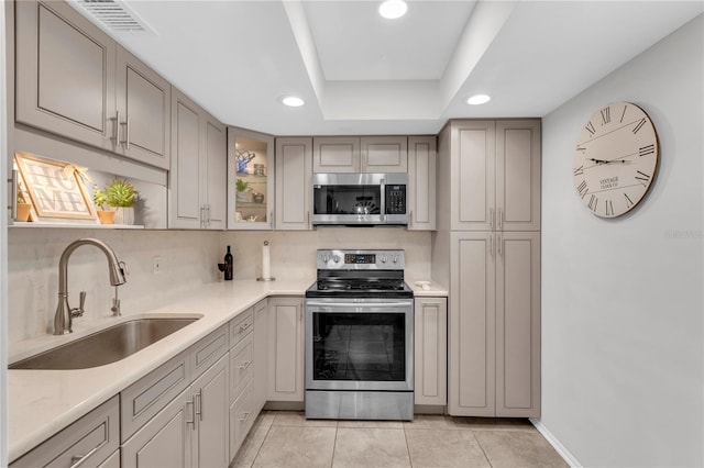 kitchen featuring tasteful backsplash, stainless steel appliances, a raised ceiling, sink, and light tile patterned floors