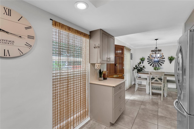 kitchen with stainless steel refrigerator, an inviting chandelier, decorative light fixtures, light tile patterned floors, and ornamental molding