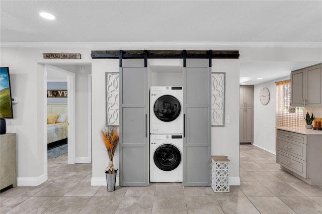 laundry room with a barn door, stacked washing maching and dryer, ornamental molding, and light tile patterned flooring