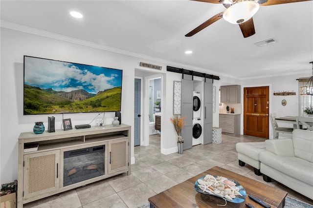 living room with a barn door, ornamental molding, stacked washer / dryer, and light tile patterned floors