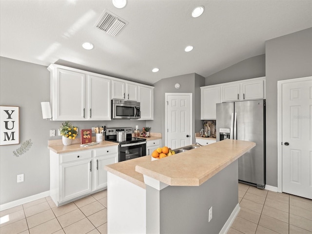 kitchen with a kitchen island with sink, vaulted ceiling, appliances with stainless steel finishes, light tile patterned flooring, and white cabinetry