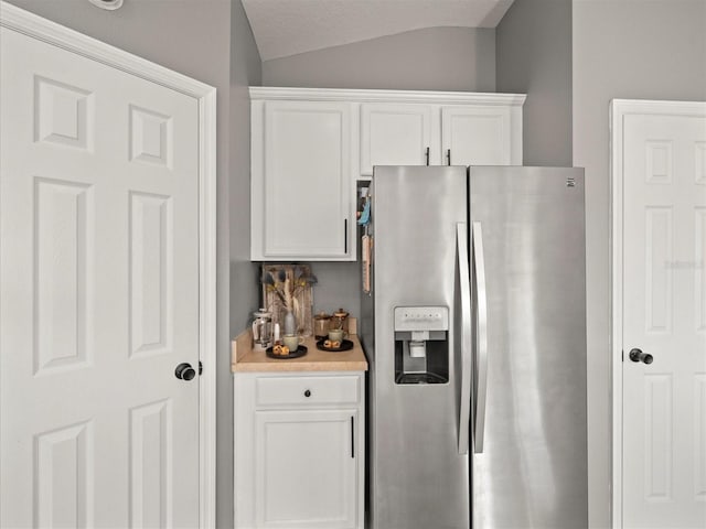 kitchen with white cabinetry, stainless steel fridge, a textured ceiling, and vaulted ceiling