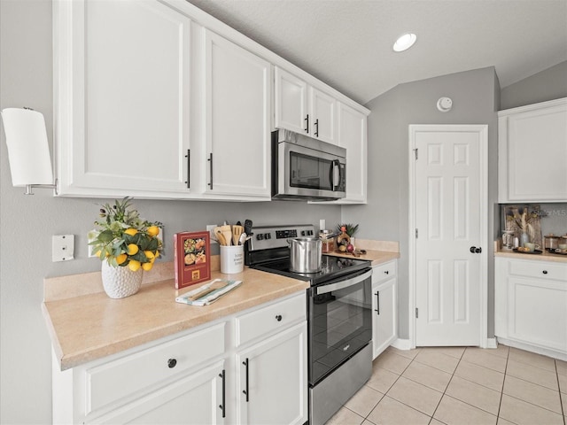 kitchen with light tile patterned floors, white cabinetry, appliances with stainless steel finishes, and vaulted ceiling