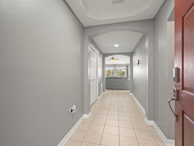 corridor with a raised ceiling and light tile patterned flooring