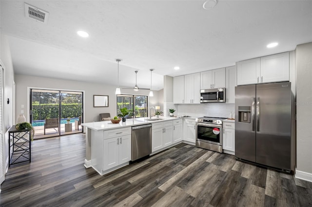 kitchen featuring kitchen peninsula, white cabinets, pendant lighting, appliances with stainless steel finishes, and dark hardwood / wood-style flooring