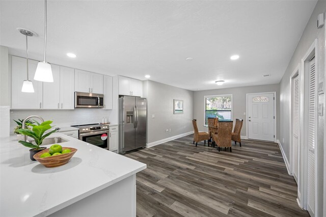 kitchen featuring dark wood-type flooring, hanging light fixtures, sink, white cabinetry, and appliances with stainless steel finishes