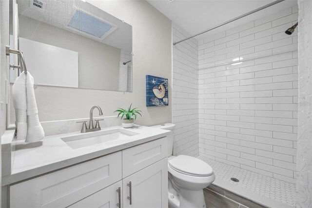 bathroom with vanity, toilet, hardwood / wood-style flooring, and tiled shower