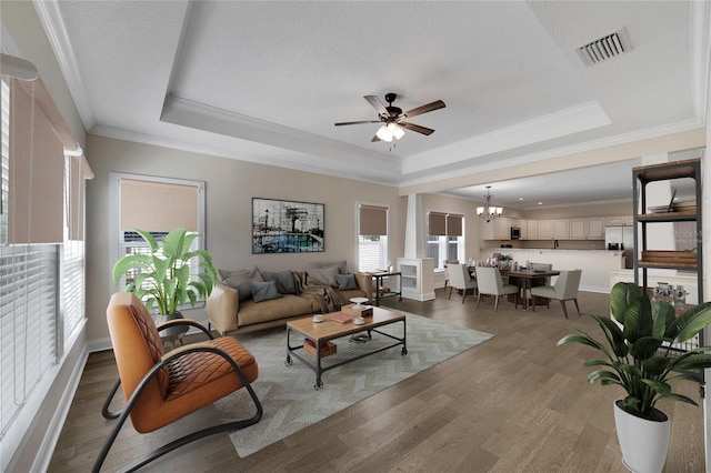 living room featuring ceiling fan with notable chandelier, crown molding, a tray ceiling, and hardwood / wood-style flooring