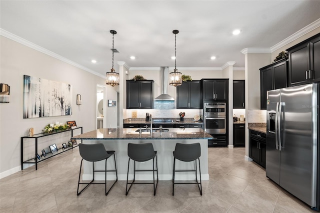 kitchen with an island with sink, wall chimney exhaust hood, stainless steel appliances, decorative light fixtures, and crown molding