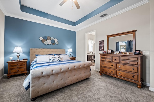 carpeted bedroom featuring ornamental molding, connected bathroom, a tray ceiling, and ceiling fan