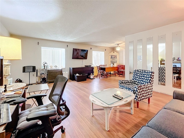 living room with light wood-type flooring, a textured ceiling, and ceiling fan