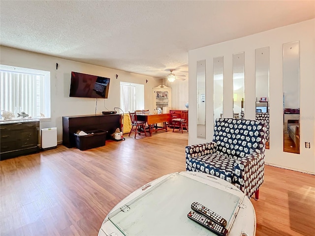 living room featuring wood-type flooring, a textured ceiling, and ceiling fan