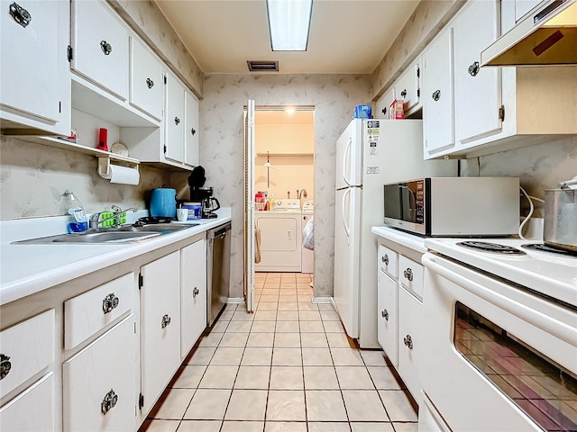 kitchen with appliances with stainless steel finishes, light tile patterned flooring, white cabinetry, and washing machine and clothes dryer