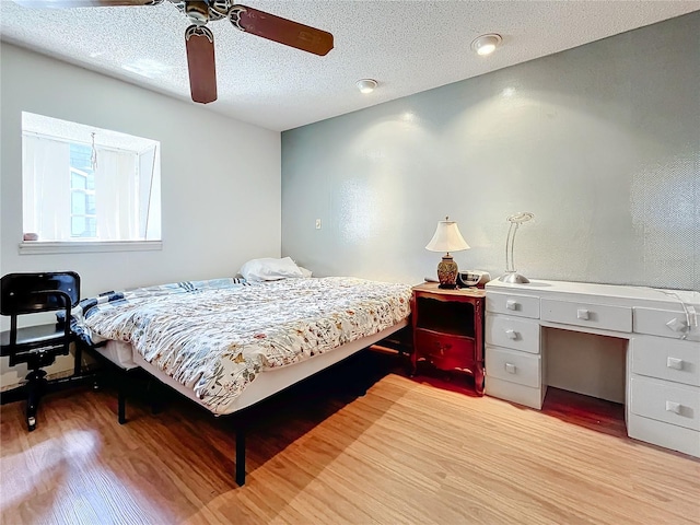 bedroom featuring built in desk, light hardwood / wood-style floors, ceiling fan, and a textured ceiling