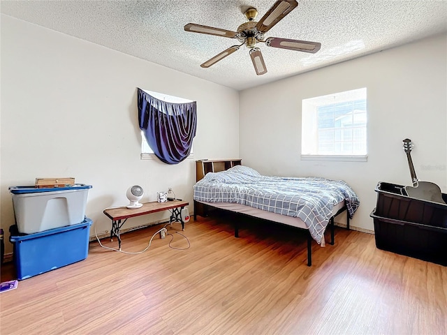 bedroom with a textured ceiling, wood-type flooring, and ceiling fan