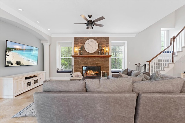 living room with a large fireplace, a ceiling fan, stairway, stone finish flooring, and crown molding