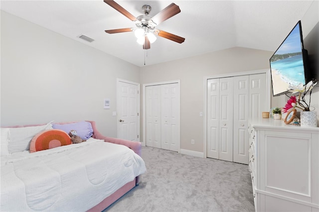 bedroom with ceiling fan, lofted ceiling, light carpet, visible vents, and multiple closets