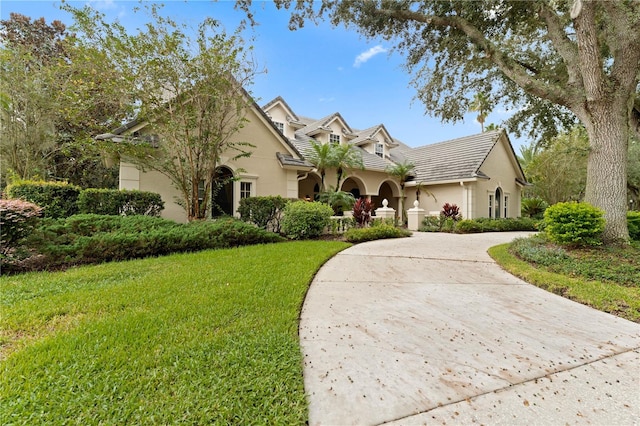 view of front of home featuring a front yard, concrete driveway, a tiled roof, and stucco siding